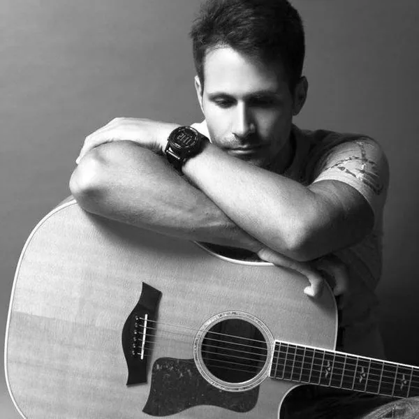 Black and white studio portrait of Stelios Antoniou with his acoustic guitar